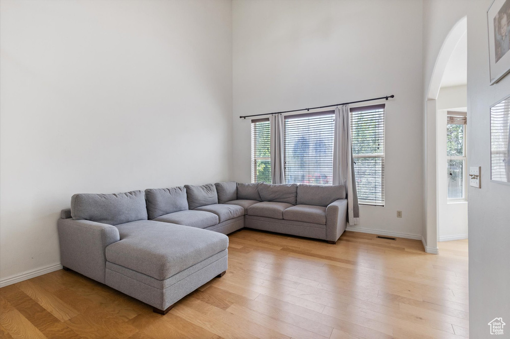 Living room with arched walkways, light wood-style floors, healthy amount of natural light, and a high ceiling