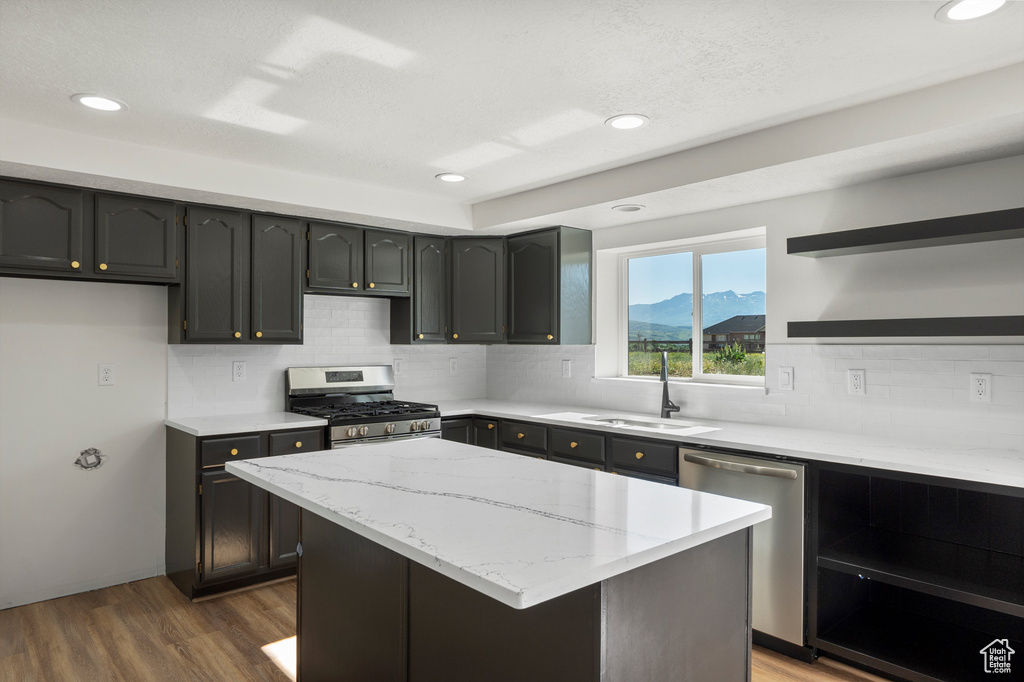 Kitchen with stainless steel appliances, open shelves, a sink, dark wood-type flooring, and light stone counters
