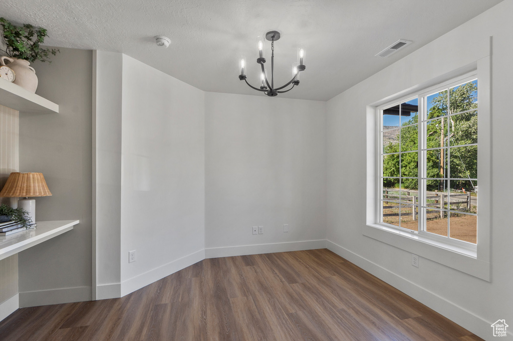 Unfurnished dining area with a chandelier, wood finished floors, and baseboards