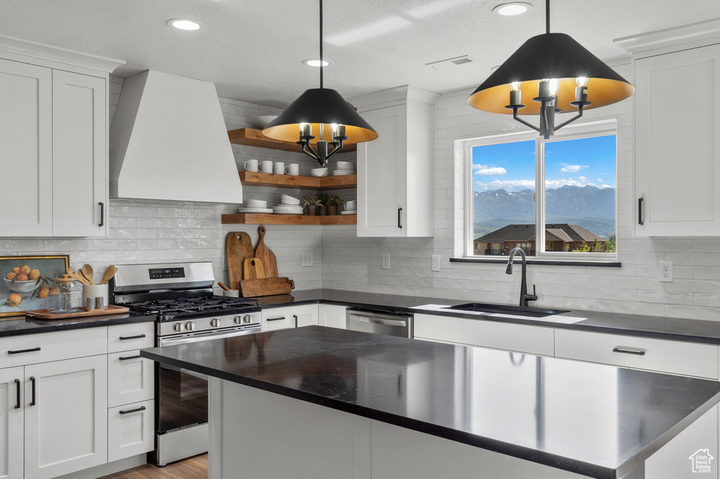 Kitchen featuring appliances with stainless steel finishes, wall chimney exhaust hood, a sink, dark countertops, and recessed lighting
