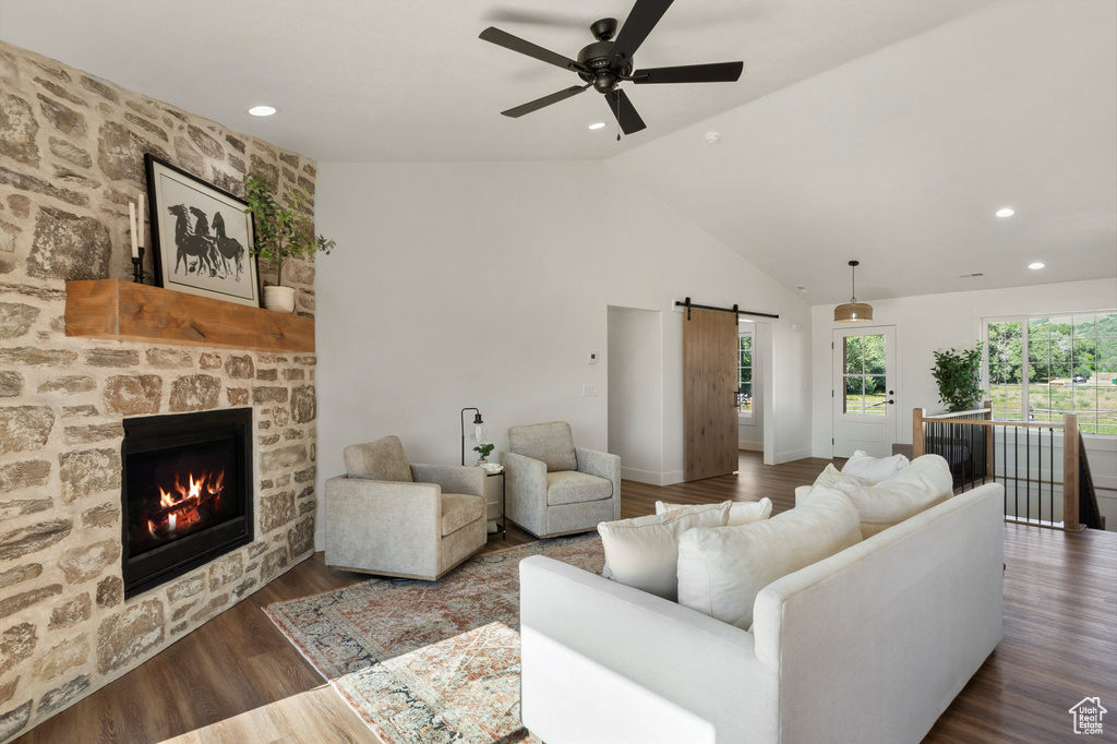 Living area featuring a barn door, high vaulted ceiling, ceiling fan, a stone fireplace, and wood finished floors
