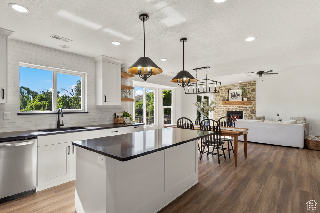 Kitchen featuring stainless steel dishwasher, a sink, dark countertops, wood finished floors, and a large fireplace