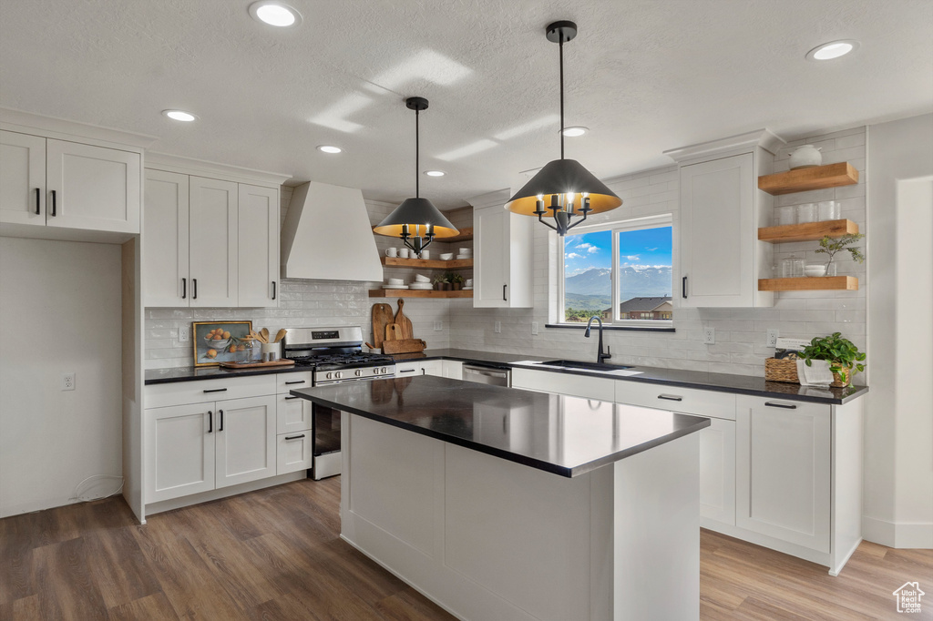 Kitchen with open shelves, appliances with stainless steel finishes, custom range hood, a sink, and dark countertops