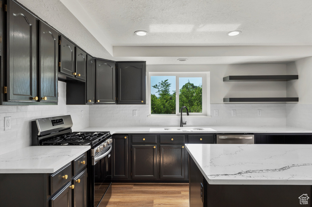 Kitchen with stainless steel appliances, a sink, open shelves, a textured ceiling, and light stone countertops