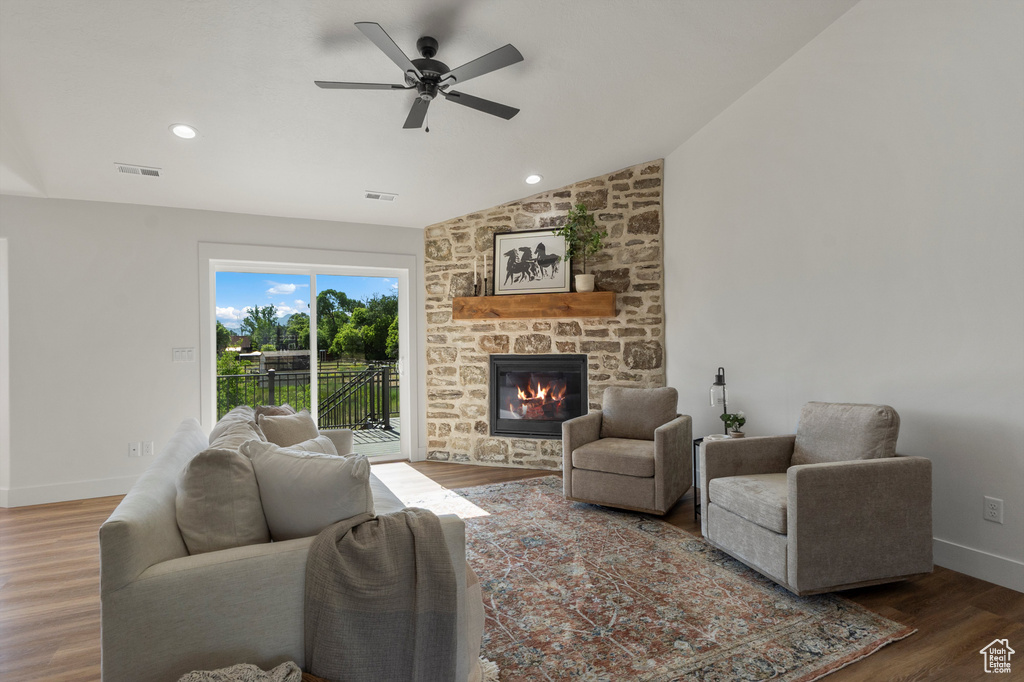 Living room featuring a stone fireplace, a ceiling fan, wood finished floors, vaulted ceiling, and baseboards