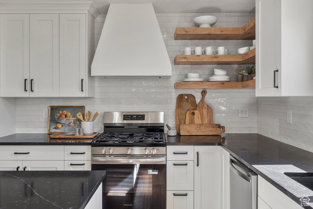Kitchen featuring stainless steel appliances, exhaust hood, backsplash, and open shelves