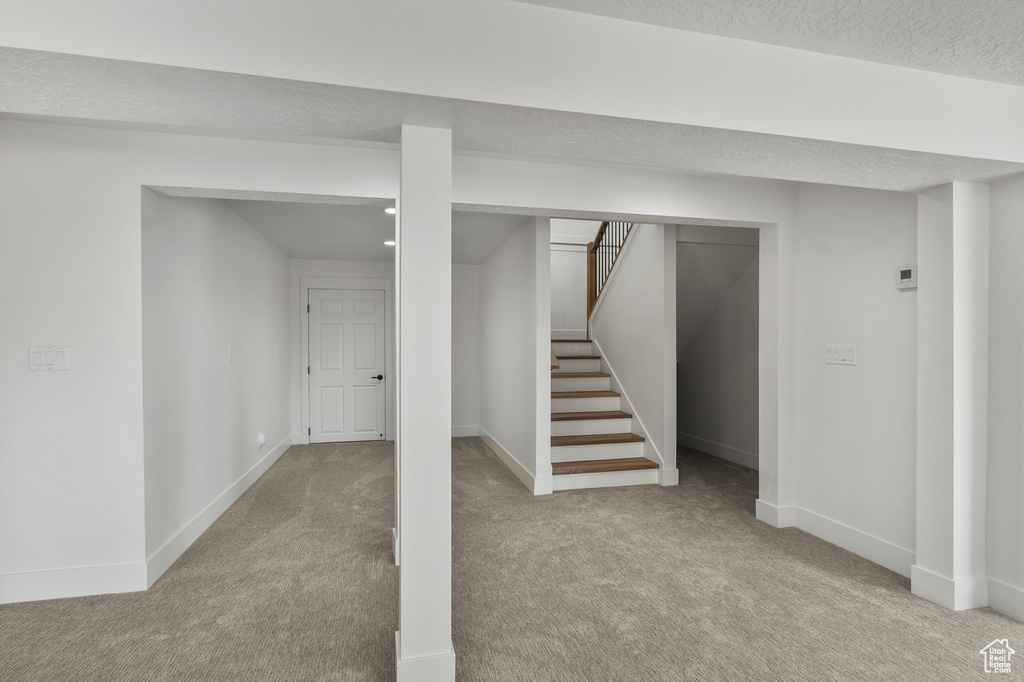 Finished below grade area featuring carpet flooring, baseboards, stairway, and a textured ceiling