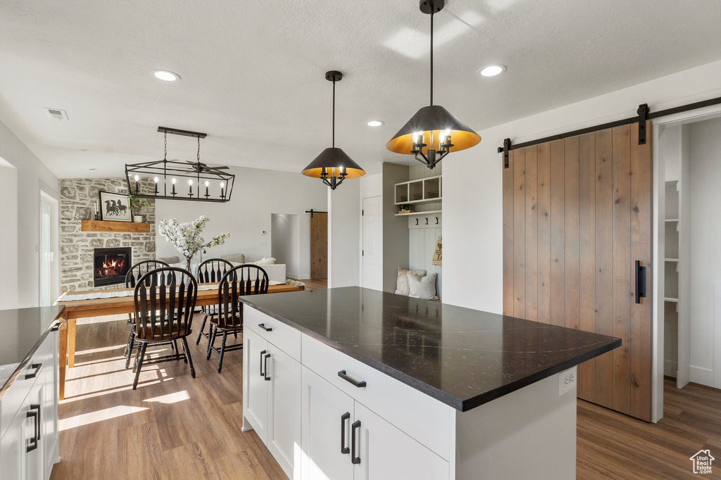Kitchen featuring wood finished floors, dark countertops, a stone fireplace, a barn door, and recessed lighting