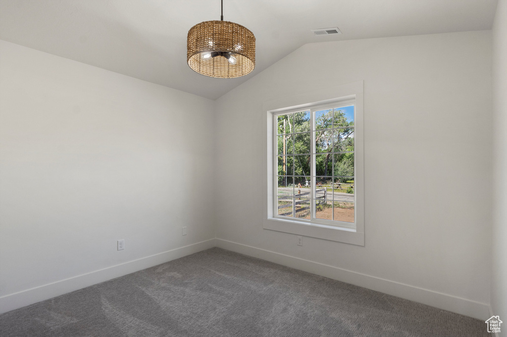 Carpeted spare room featuring vaulted ceiling, baseboards, and a chandelier