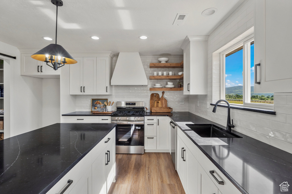 Kitchen with stainless steel appliances, premium range hood, a sink, open shelves, and white cabinets