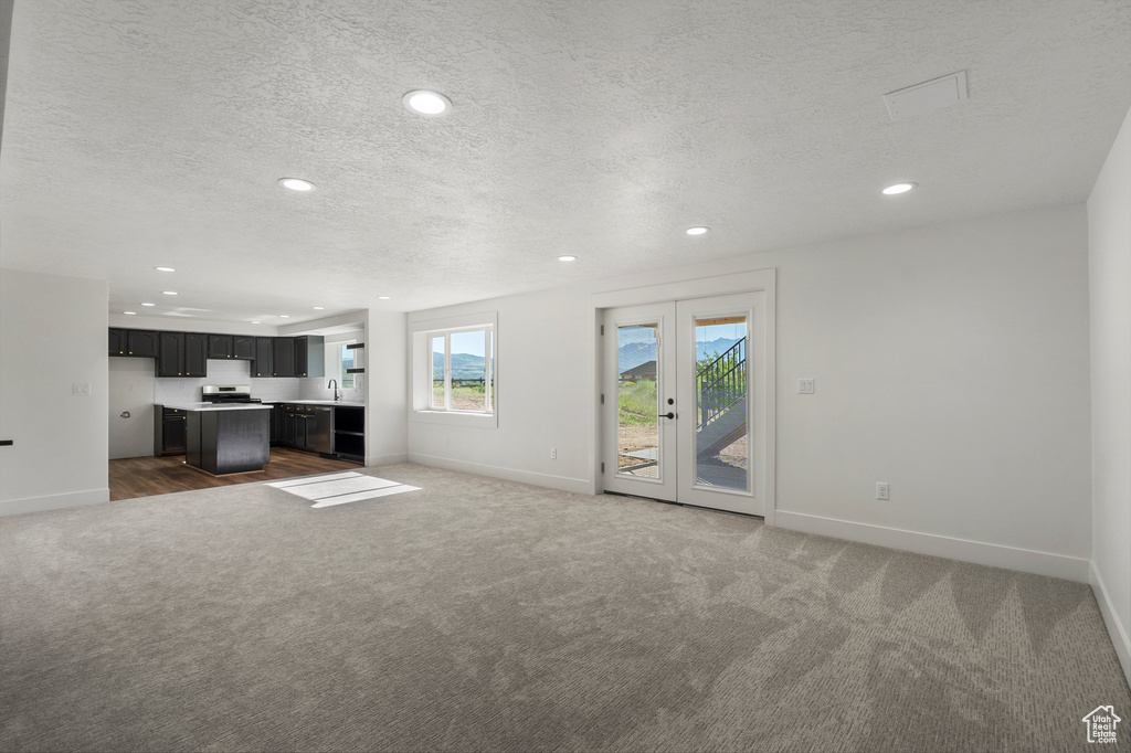 Unfurnished living room featuring carpet floors, baseboards, a textured ceiling, recessed lighting, and a sink