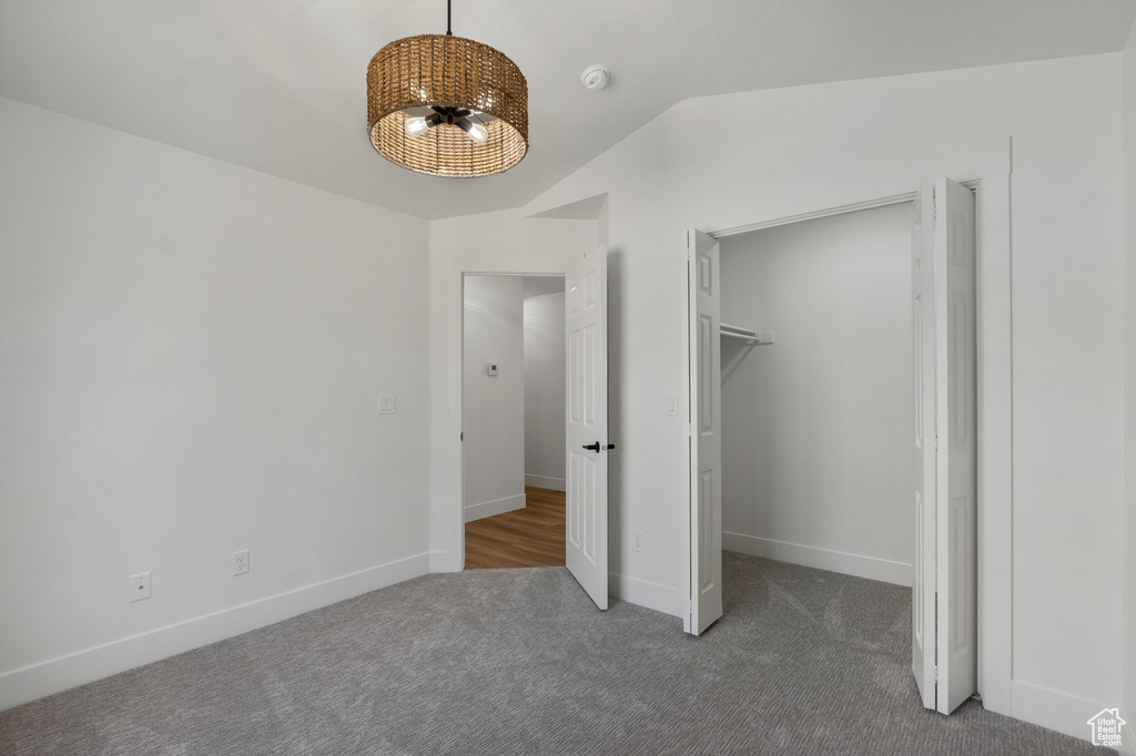 Unfurnished bedroom with carpet flooring, a chandelier, lofted ceiling, baseboards, and a spacious closet