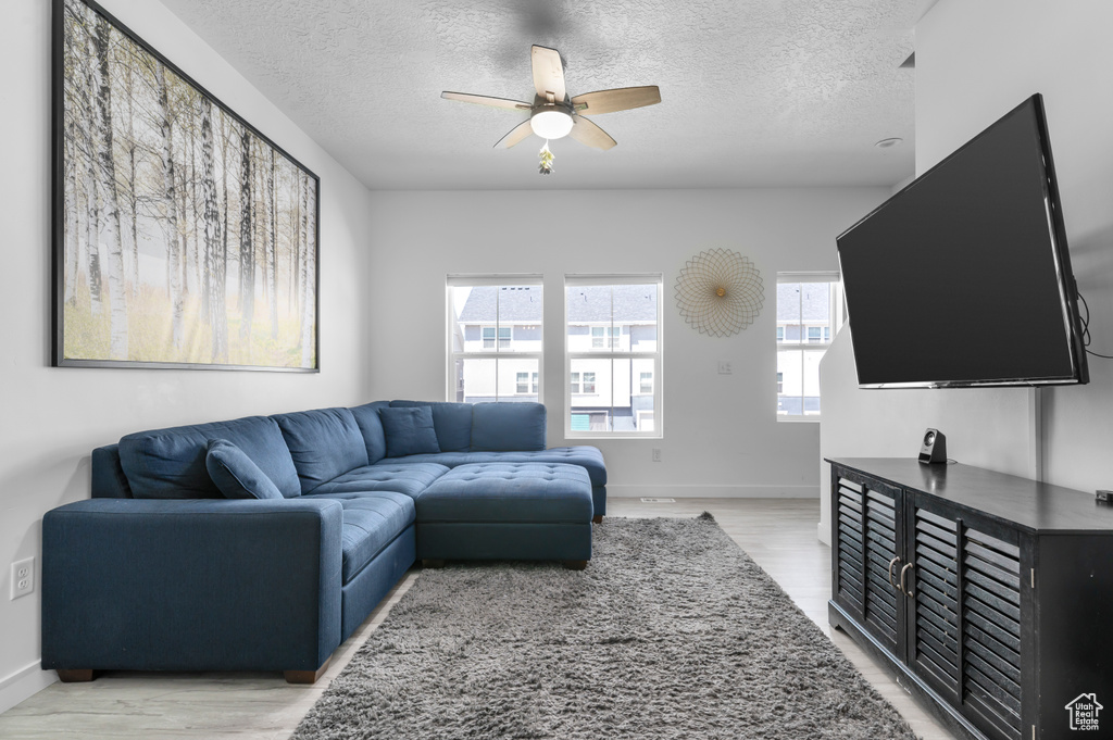 Living area featuring a textured ceiling, a ceiling fan, light wood-style floors, and baseboards