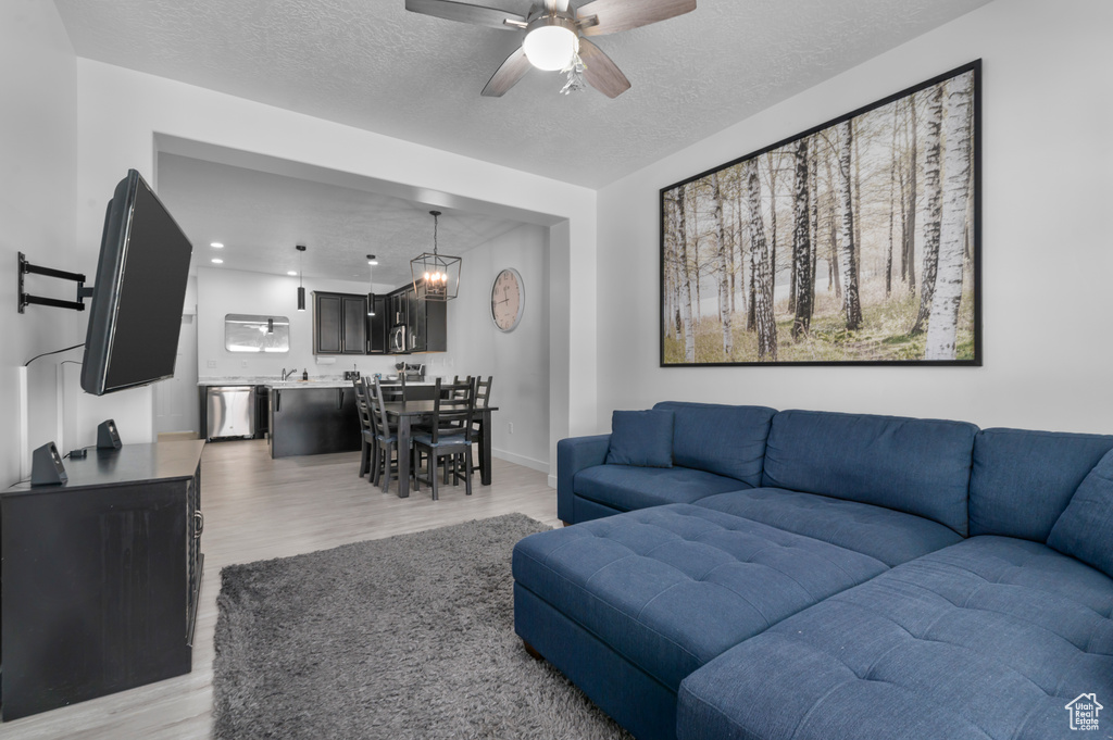 Living room with light wood finished floors, ceiling fan, a textured ceiling, and baseboards