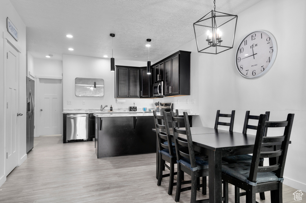 Dining room featuring light wood finished floors, a chandelier, baseboards, recessed lighting, and a textured ceiling