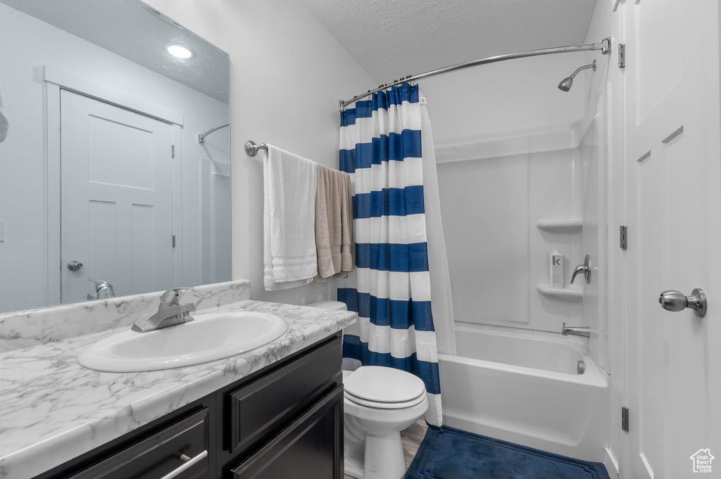 Bathroom with vanity, shower / bathtub combination with curtain, toilet, and a textured ceiling