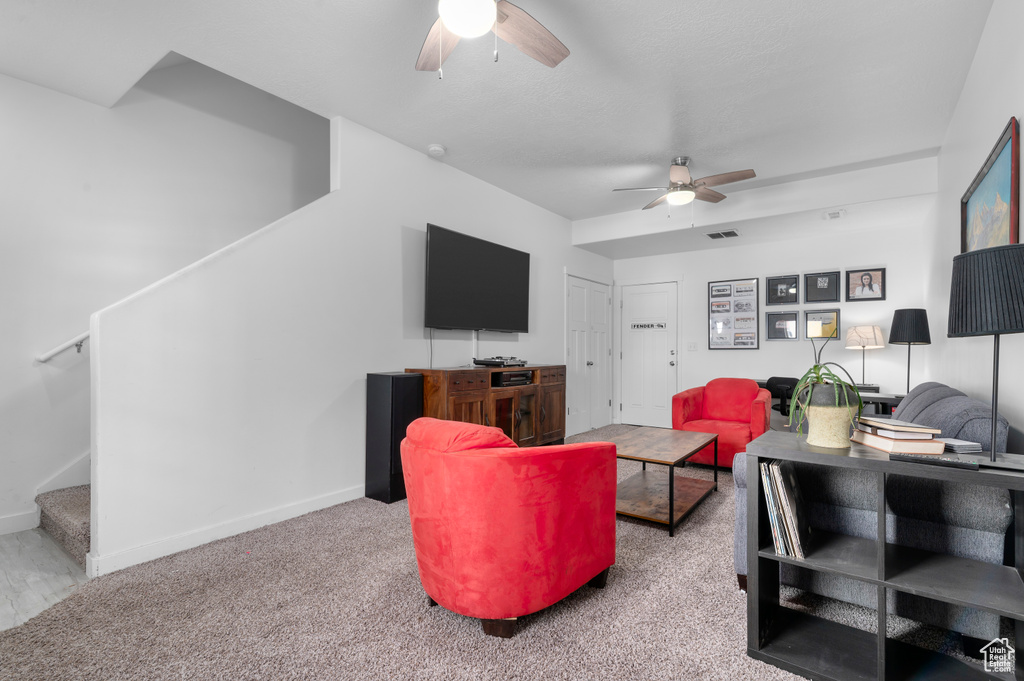 Carpeted living area featuring ceiling fan, stairs, and baseboards