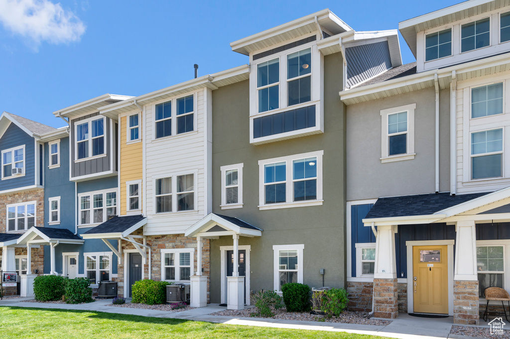 Townhome / multi-family property with stone siding, stucco siding, and central AC unit