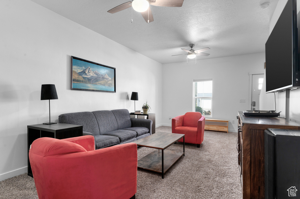 Living room with a ceiling fan, carpet, baseboards, and a textured ceiling