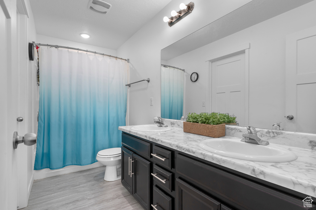 Full bathroom with double vanity, toilet, and wood finished floors