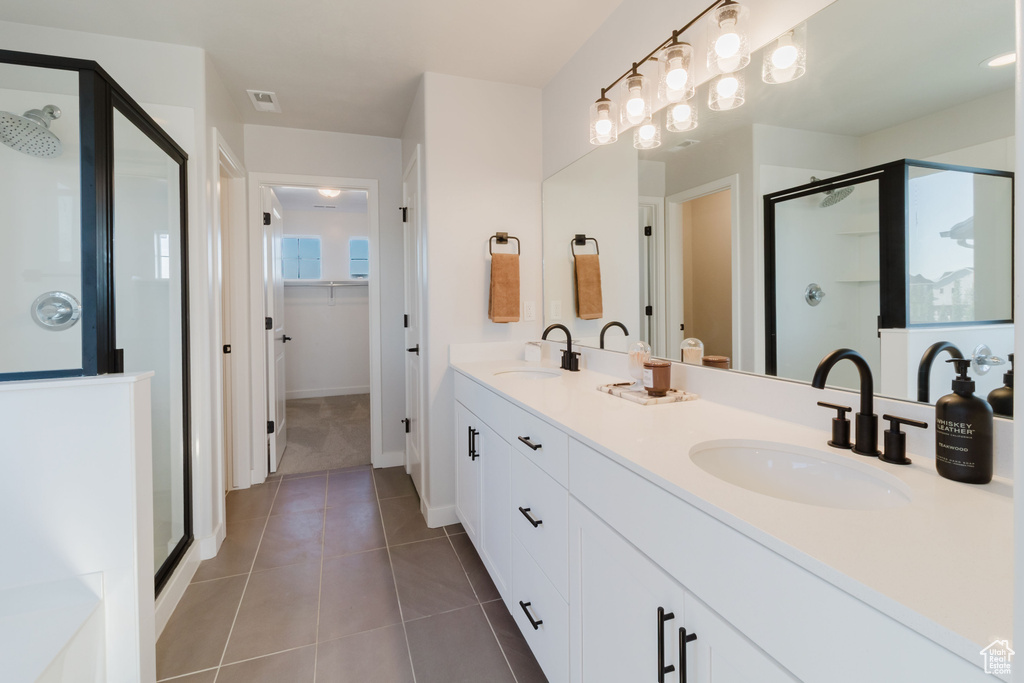 Bathroom featuring a shower stall, double vanity, tile patterned flooring, and baseboards