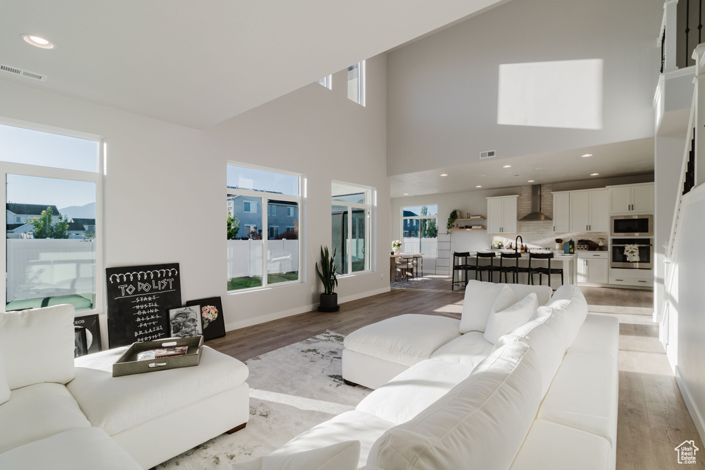 Living room with healthy amount of natural light, light wood-type flooring, a high ceiling, and recessed lighting