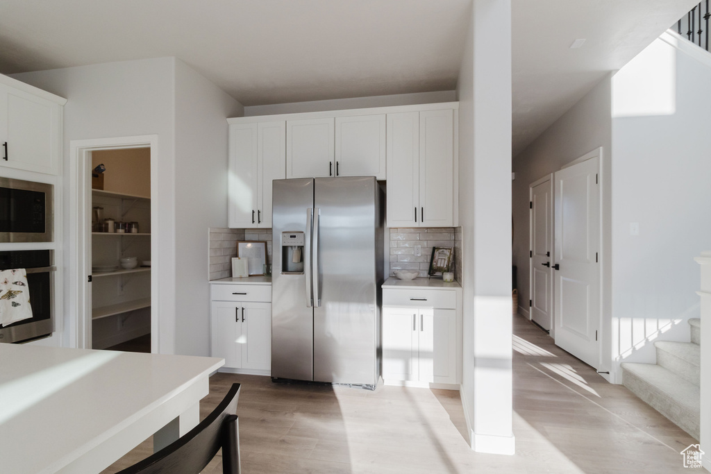 Kitchen with appliances with stainless steel finishes, light wood-style flooring, decorative backsplash, and white cabinets