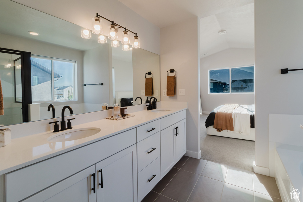 Ensuite bathroom with double vanity, a bathtub, tile patterned floors, and vaulted ceiling