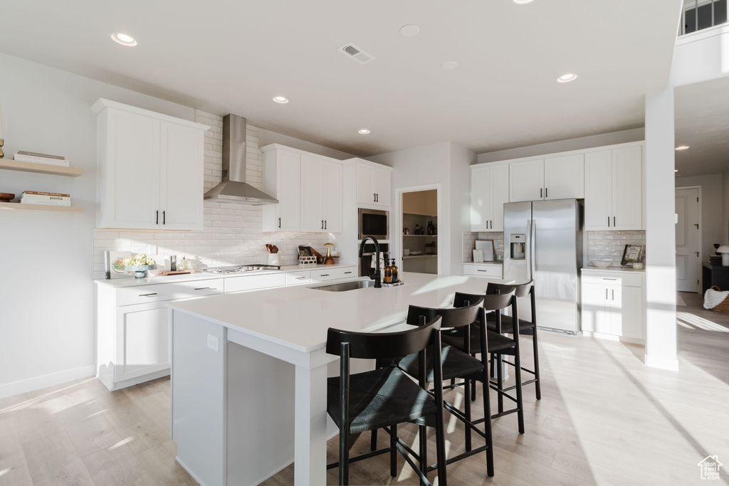Kitchen with wall chimney range hood, appliances with stainless steel finishes, a sink, tasteful backsplash, and a kitchen island with sink