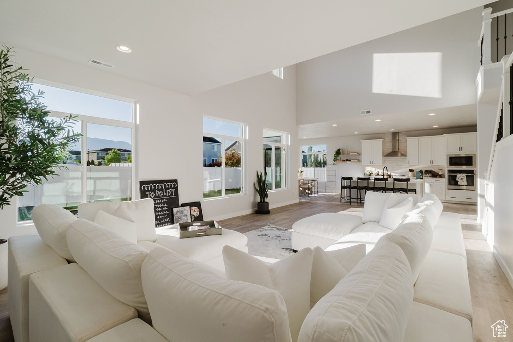 Living room with light wood-style flooring, a towering ceiling, baseboards, and recessed lighting