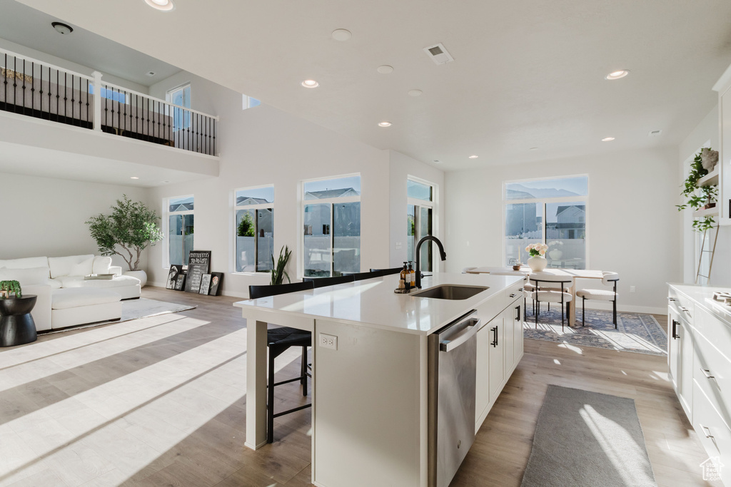 Kitchen with a sink, stainless steel dishwasher, light wood-style flooring, a center island with sink, and recessed lighting