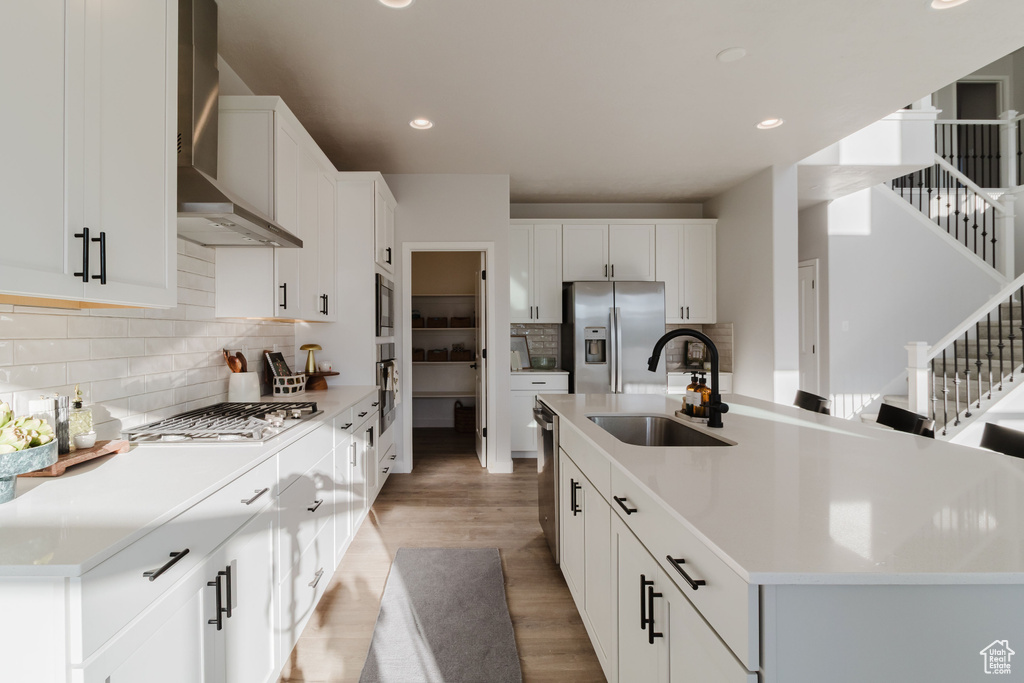 Kitchen with wall chimney range hood, appliances with stainless steel finishes, a sink, light wood-style floors, and recessed lighting