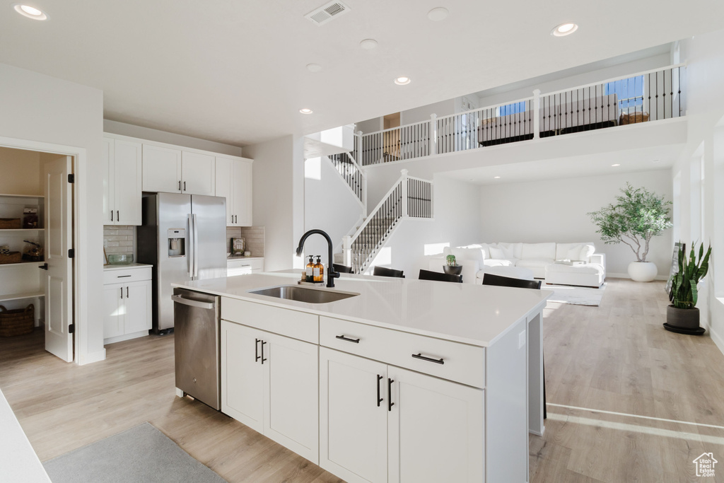 Kitchen featuring appliances with stainless steel finishes, a sink, a kitchen island with sink, light wood-type flooring, and white cabinetry