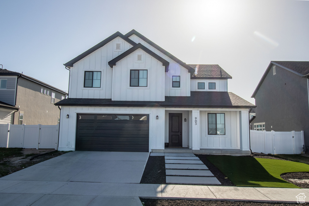Modern inspired farmhouse featuring board and batten siding, an attached garage, concrete driveway, and a gate