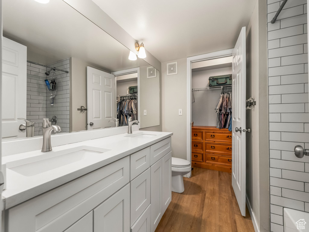 Bathroom with double vanity, a spacious closet, wood finished floors, toilet, and a shower