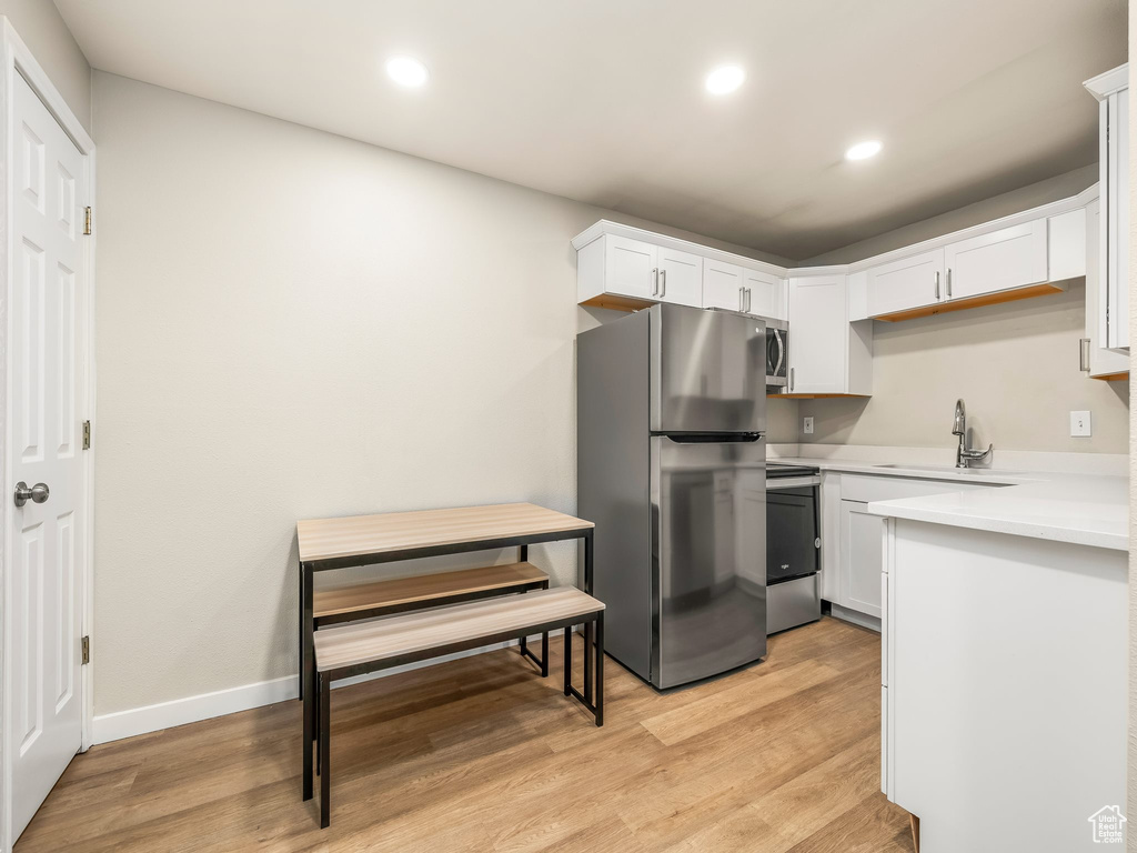 Kitchen featuring stainless steel appliances, a sink, white cabinets, light countertops, and light wood finished floors