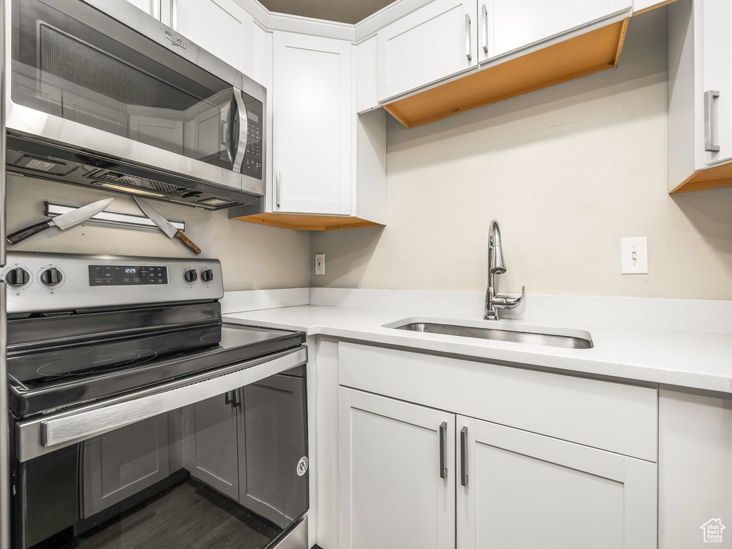 Kitchen featuring appliances with stainless steel finishes, a sink, white cabinets, and light countertops