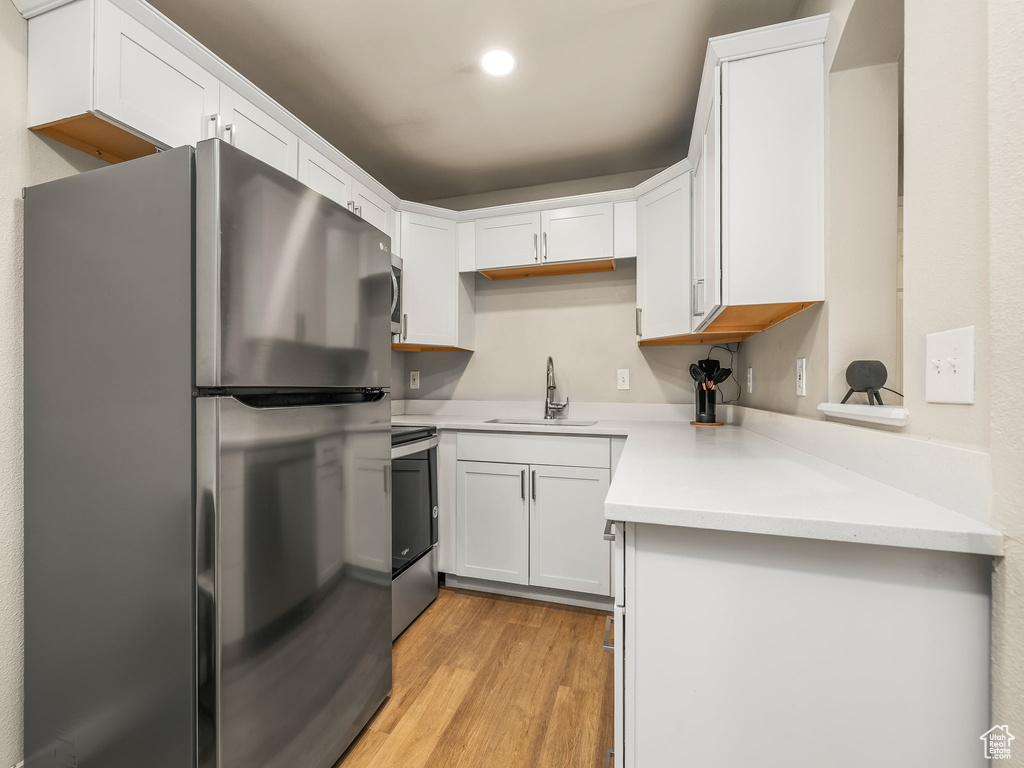 Kitchen featuring stainless steel appliances, a sink, light wood-type flooring, light countertops, and white cabinetry