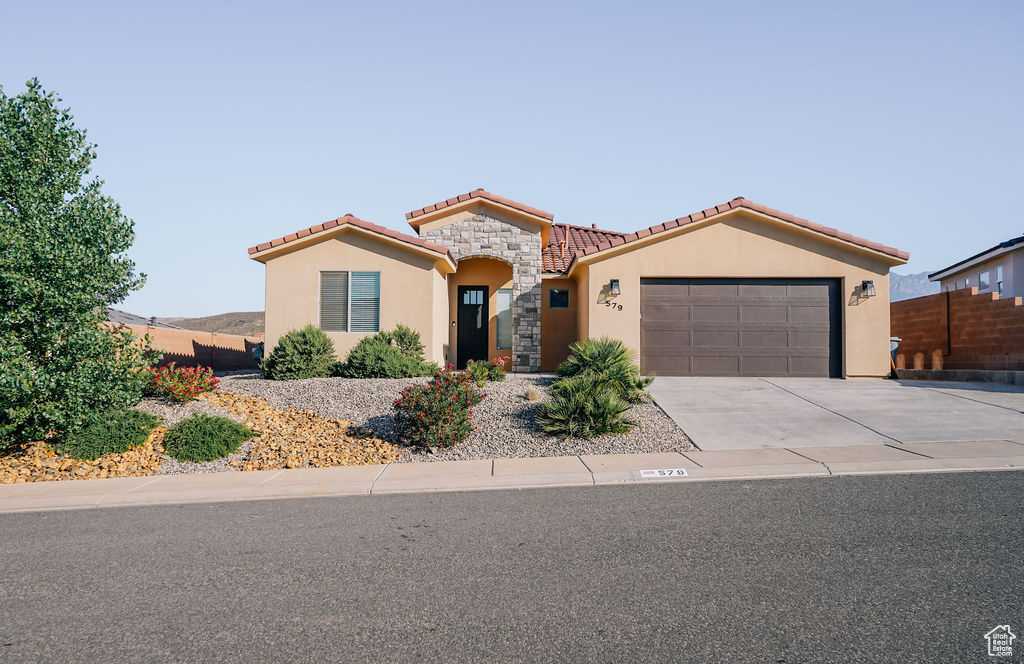 Mediterranean / spanish-style house with stucco siding, a tile roof, an attached garage, driveway, and stone siding