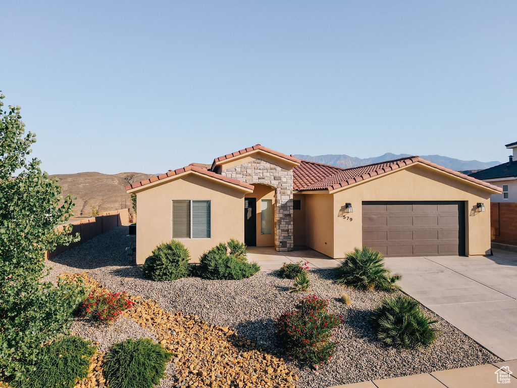 Mediterranean / spanish-style home with stucco siding, a tile roof, an attached garage, a mountain view, and driveway