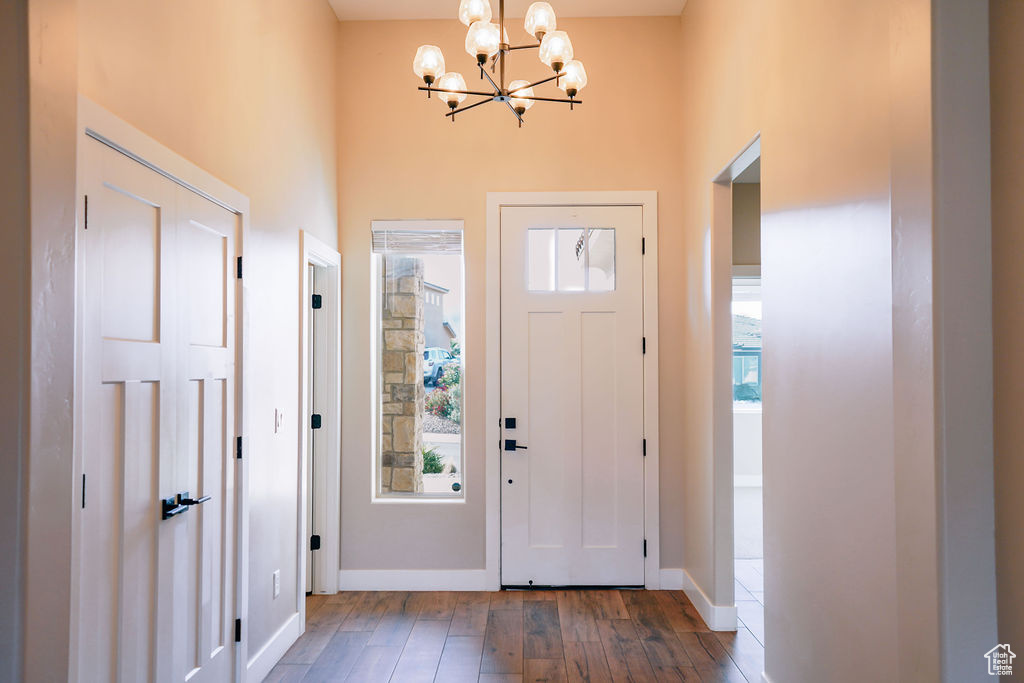 Foyer entrance with a chandelier, wood-type flooring, a high ceiling, and baseboards