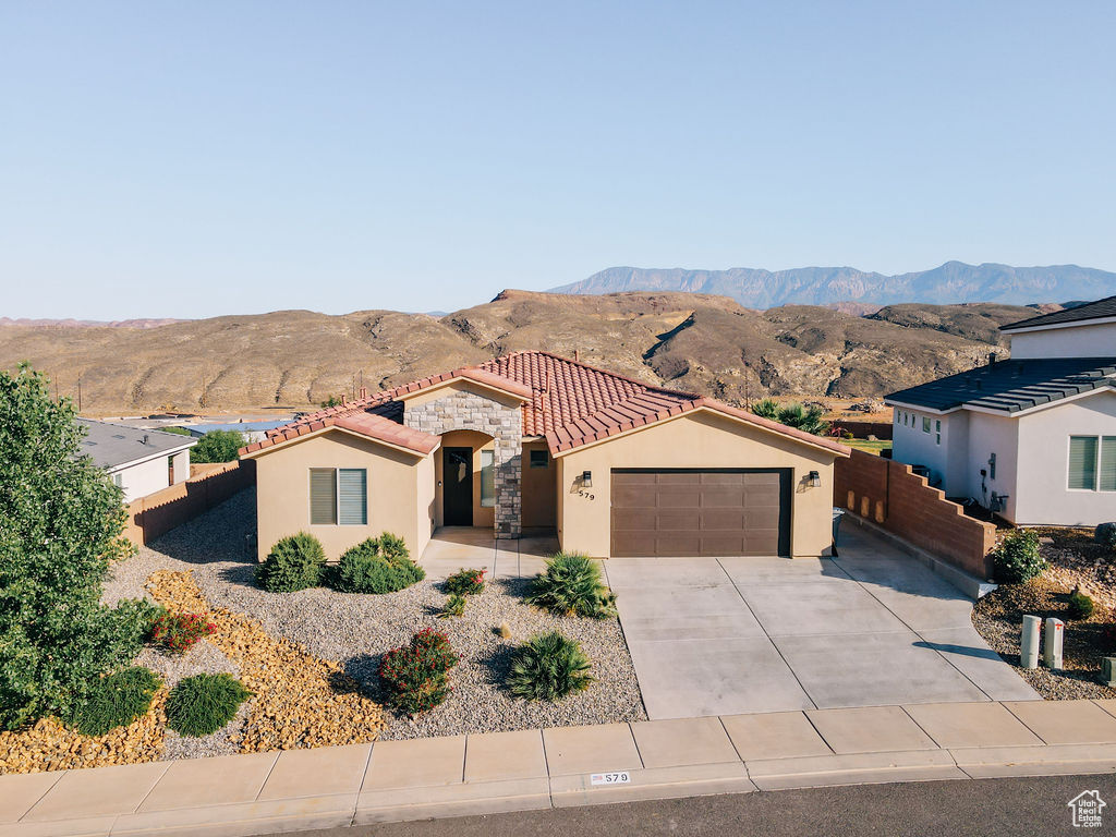 Mediterranean / spanish house featuring an attached garage, stucco siding, a mountain view, a tile roof, and driveway