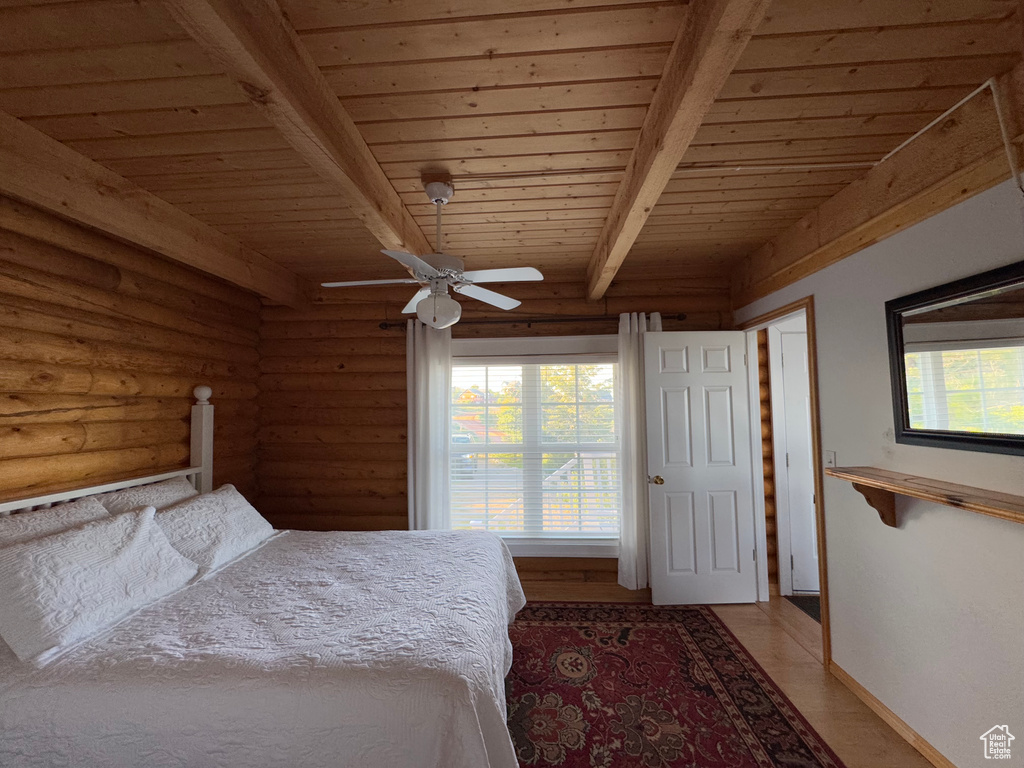 Bedroom featuring a wooden ceiling with exposed beams, rustic walls, light wood finished floors, and ceiling fan