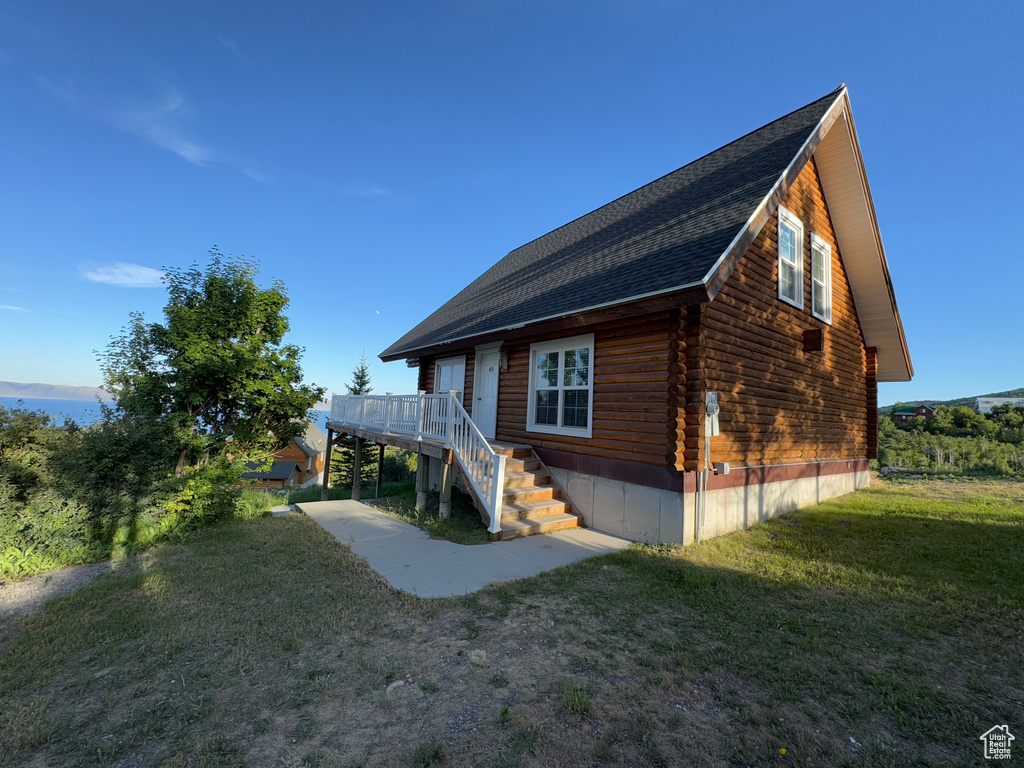 View of side of home featuring log siding, a lawn, stairs, a wooden deck, and roof with shingles