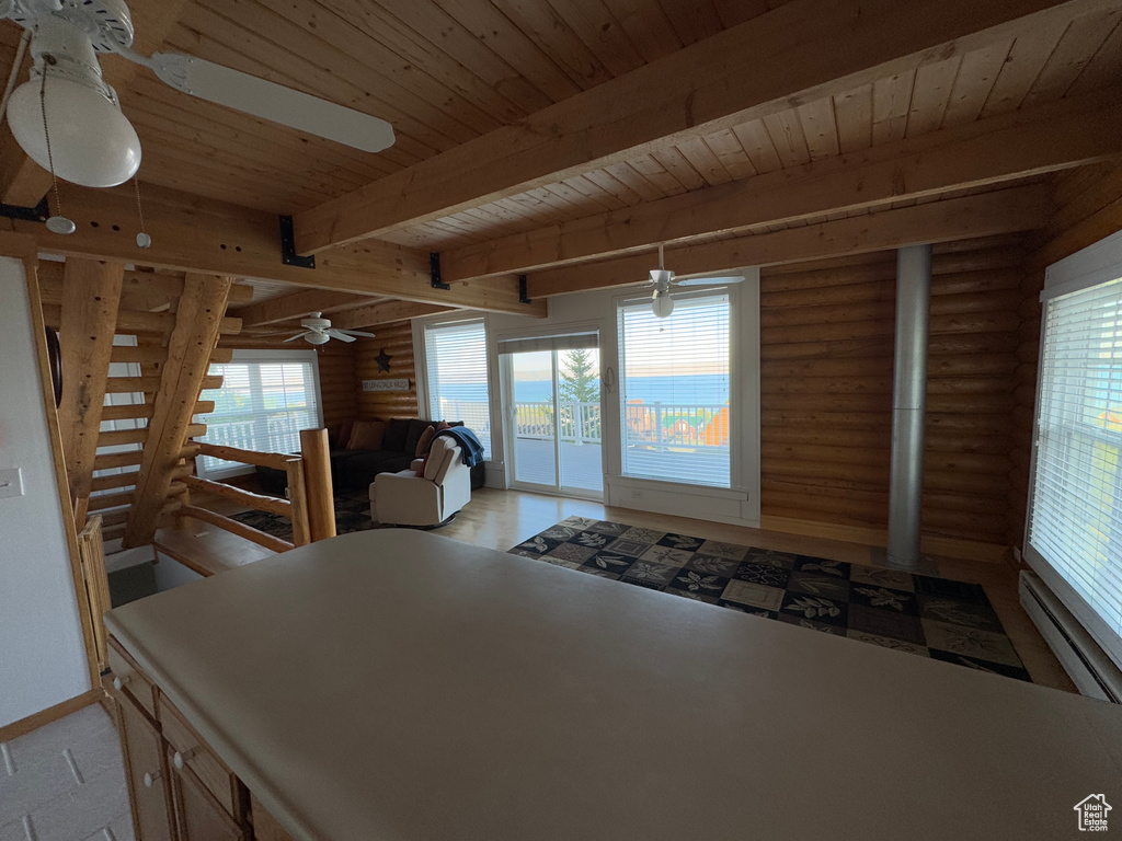 Kitchen featuring log walls, a wood ceiling with exposed beams, plenty of natural light, a ceiling fan, and a baseboard radiator