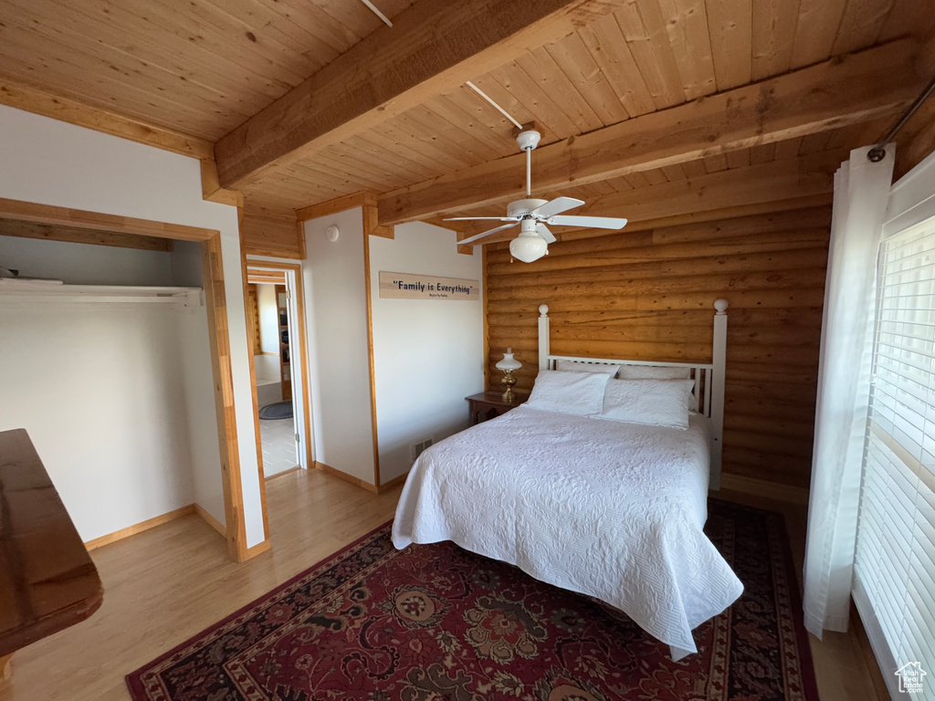 Bedroom featuring a wood ceiling with exposed beams, rustic walls, wood finished floors, a closet, and ceiling fan