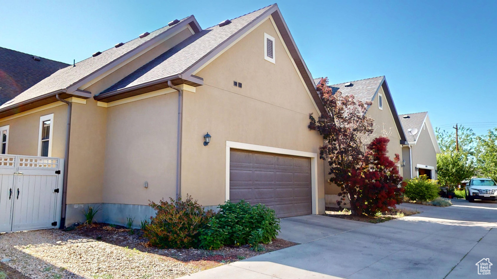 View of side of property with concrete driveway, stucco siding, roof with shingles, and a gate