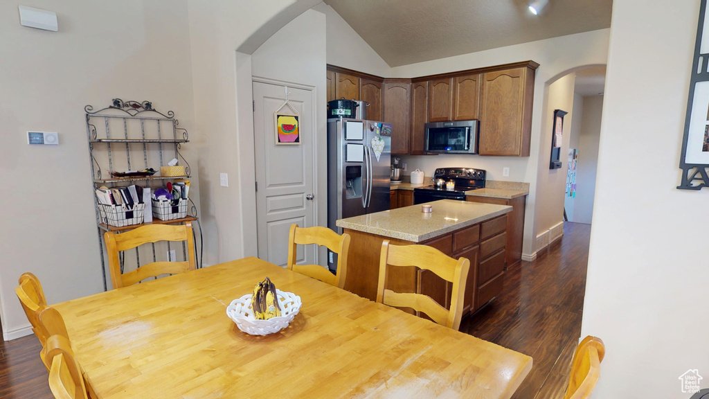 Dining space with arched walkways, dark wood finished floors, vaulted ceiling, and baseboards