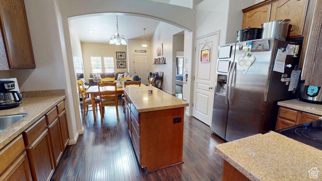 Kitchen featuring arched walkways, a center island, stainless steel refrigerator with ice dispenser, dark wood finished floors, and brown cabinetry