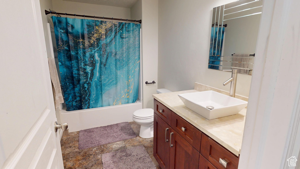 Full bath with vanity, toilet, shower / tub combo, and stone finish floors